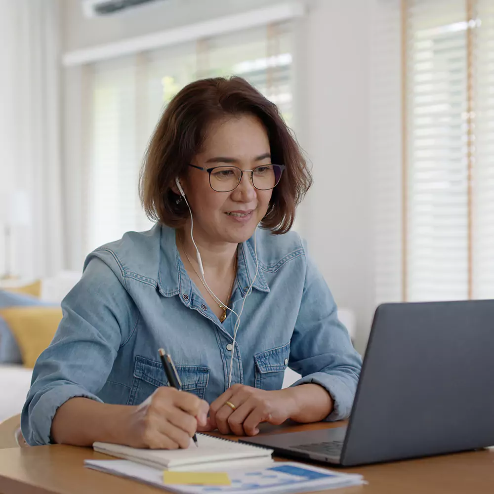 Happy woman with earphones in looking at laptop and taking notes