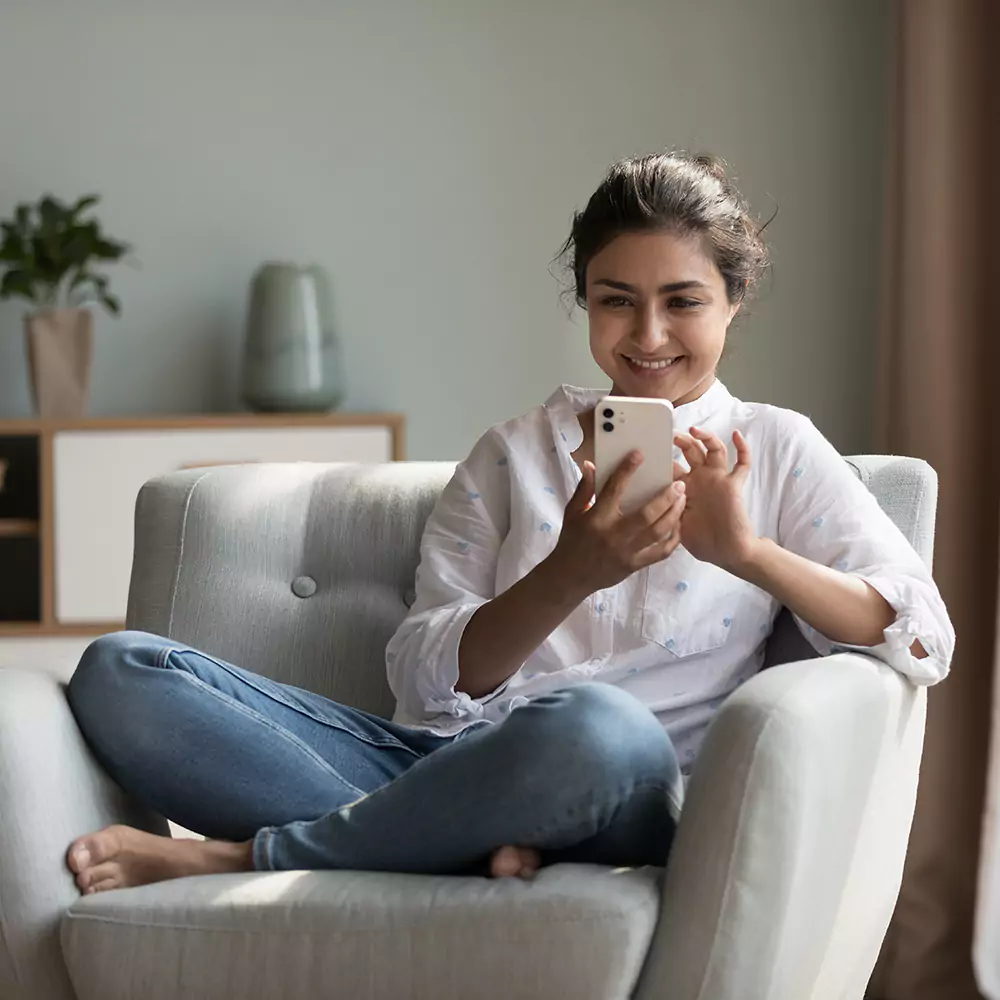 Happy woman sitting on couch at home using mobile phone to make an NDIS referral